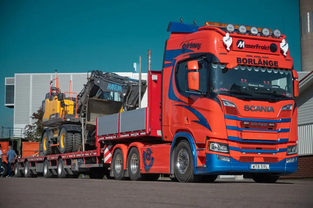 Orange lastbil från MaserFrakt som transporterar en gul grävmaskin