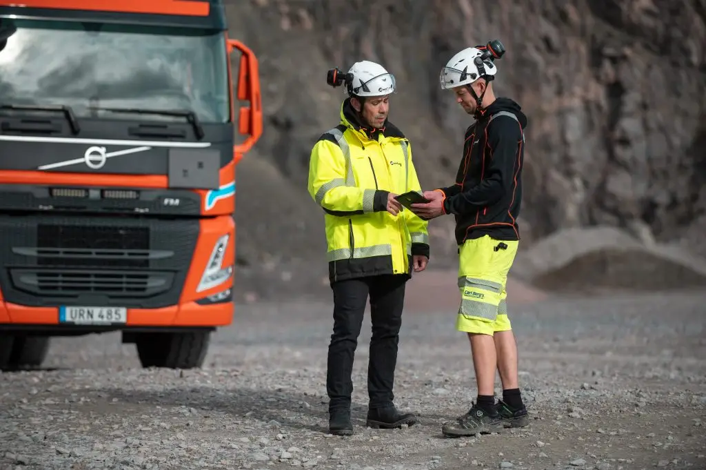 Två anställda som pratar framför en orange lastbil i MaserFrakts täkt